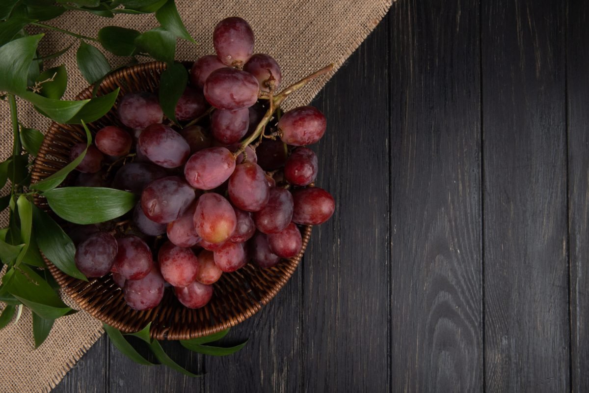 top view of a bunch of fresh sweet grapes in a wicker basket on wooden background with copy space
